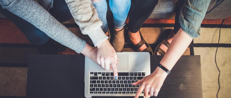 Students huddled together looking at a university website on a laptop