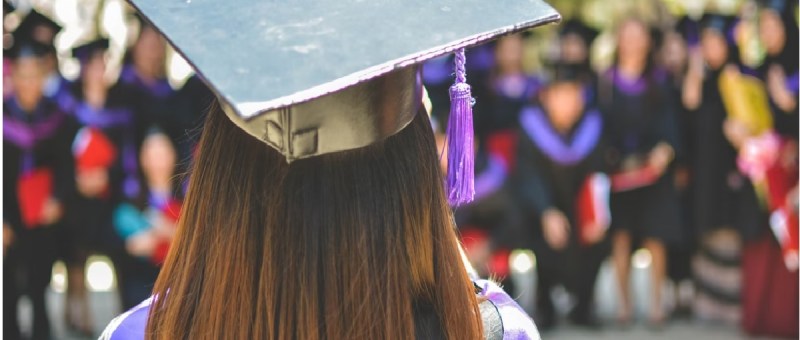 Image back of student in graduation gown, facing an audience.